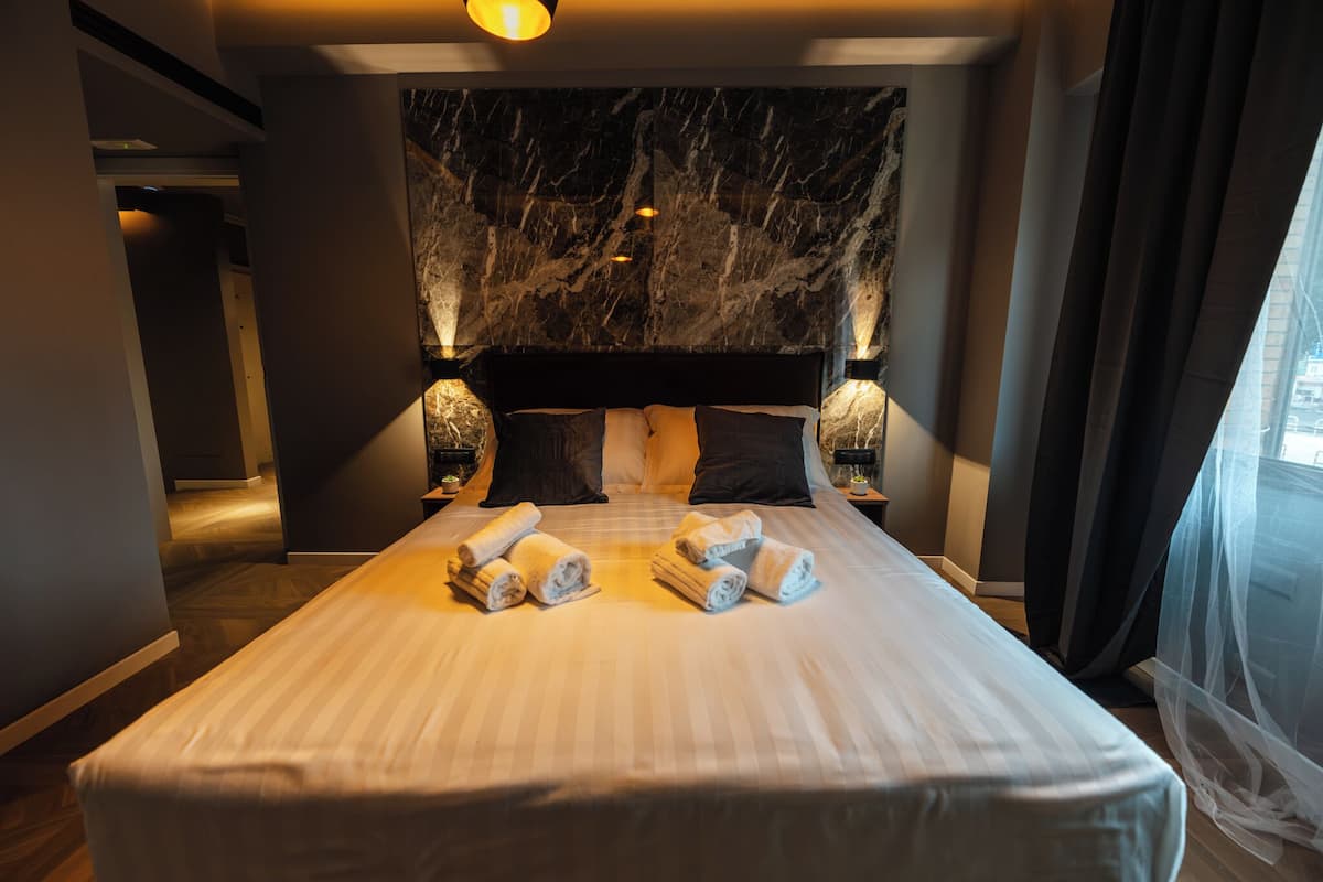 A modern hotel room with a marble headboard, a neatly made bed with towels, and ambient lighting.