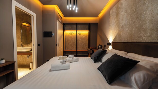 A modern hotel room with a large bed, a bathroom with a sink and mirror, a desk, and a large mirror on the wall. - Whim Collection Trastevere (Rome)