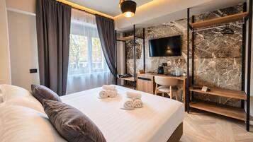 A modern hotel room with a bed, a desk, a TV, and a wardrobe.