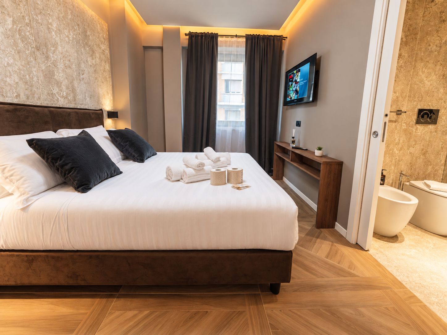 A hotel room with a large bed, a TV, a bathroom, and a view of the city.