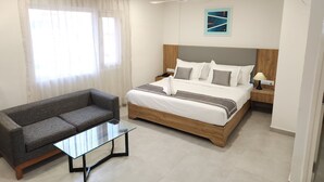 A hotel room with a bed, a grey sofa, a glass coffee table, and a ceiling fan. - OASIS SUITES (Hubli)