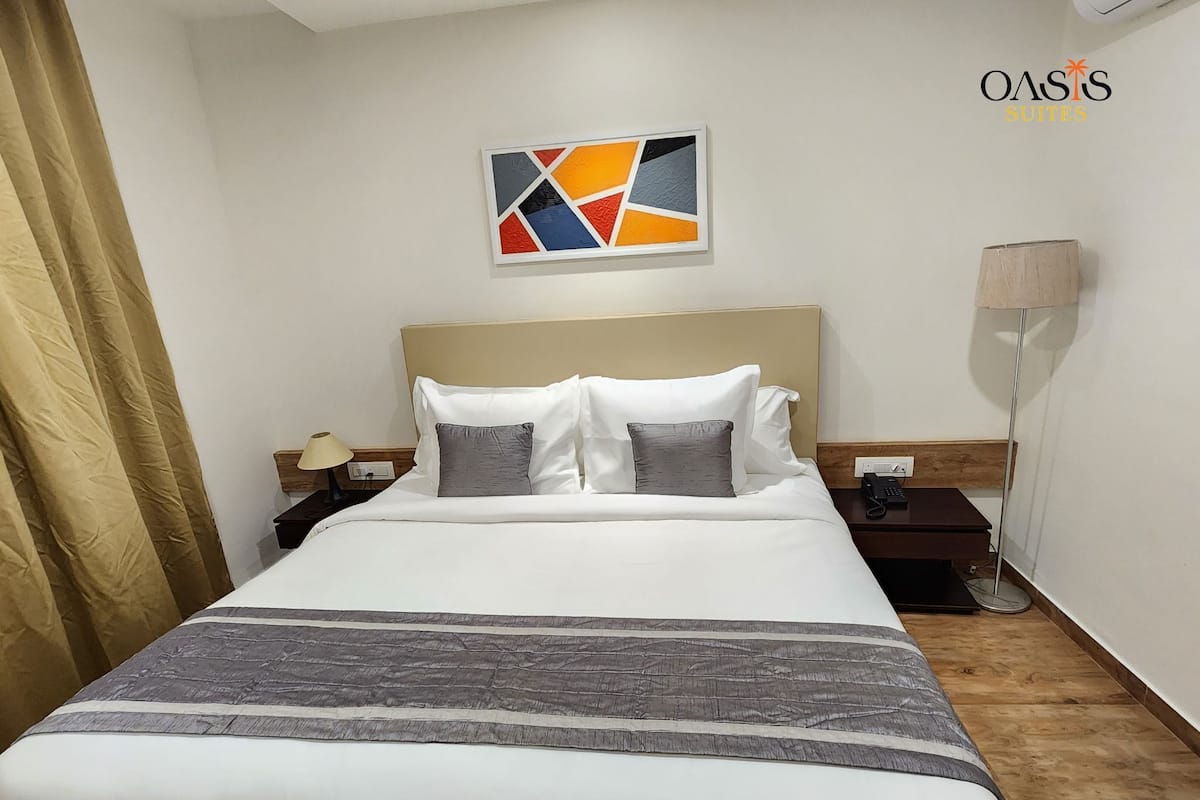 A hotel room with a bed, a nightstand, a lamp, and a painting on the wall.