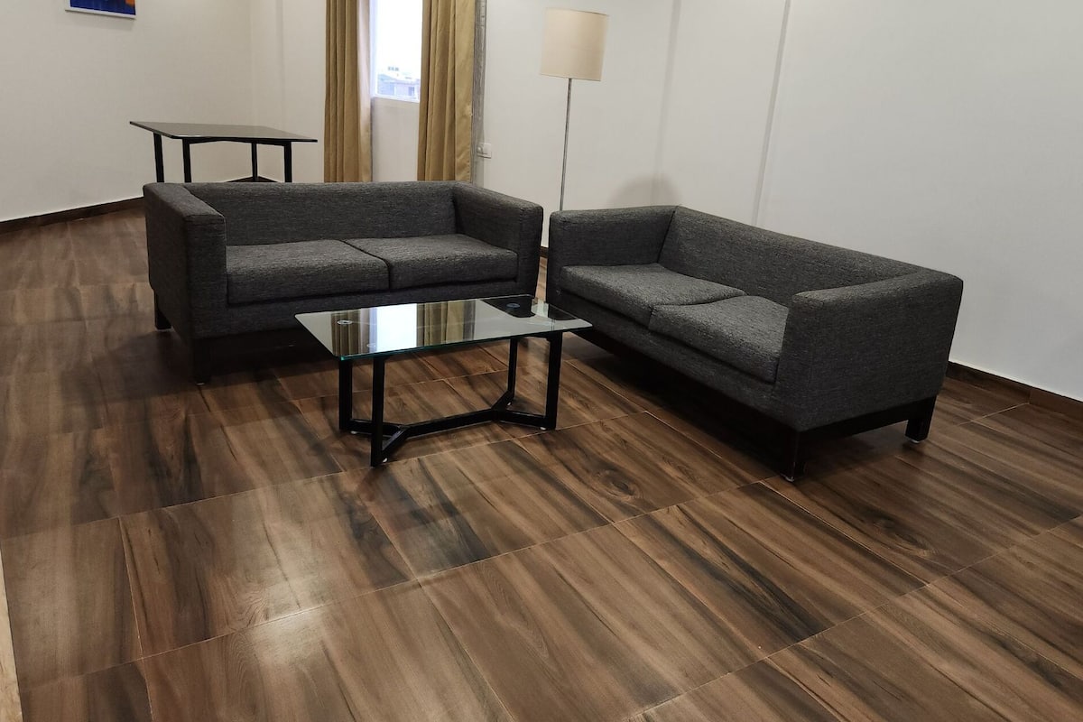 A room with two grey sofas, a glass coffee table, a small table, and a floor lamp.