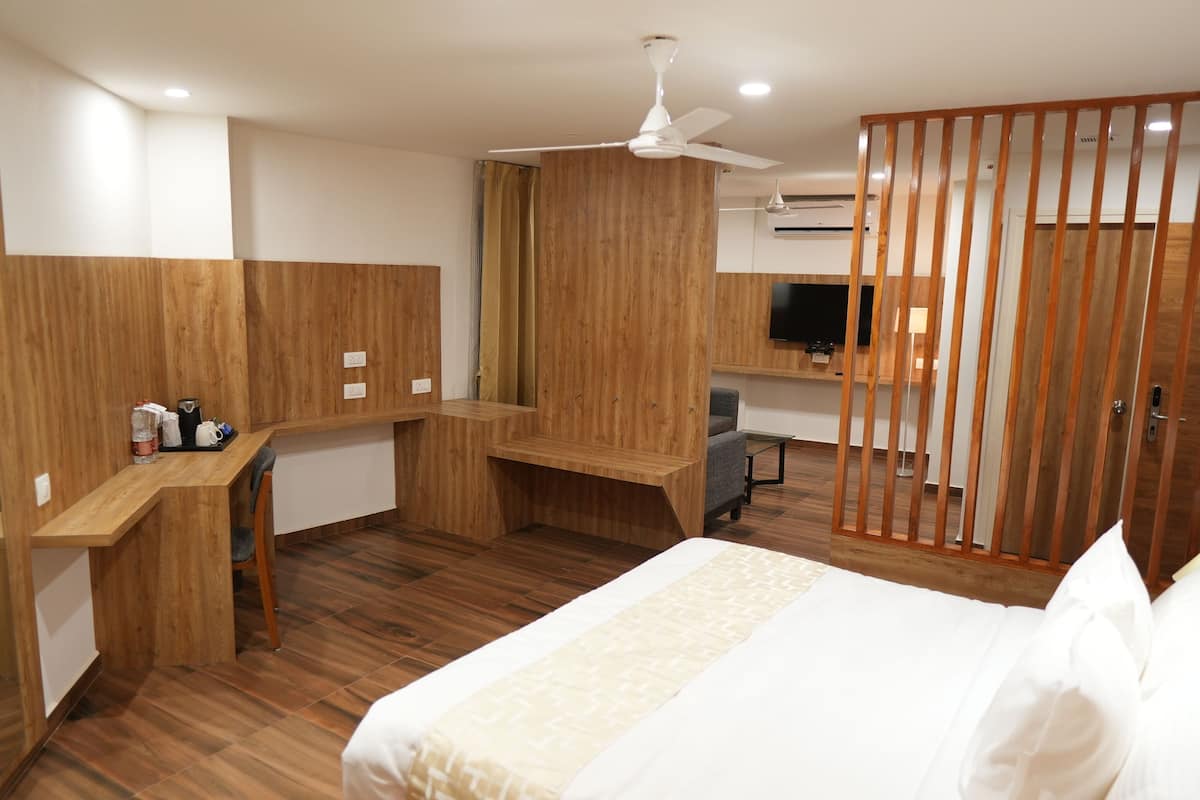 A hotel room with a bed, a desk, a chair, a ceiling fan, and a TV.