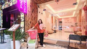 Ein Hotel Eingang mit einer Neonreklame, einem Empfangsbereich und einem Kinderwagen mit einem rosa Ventilator.