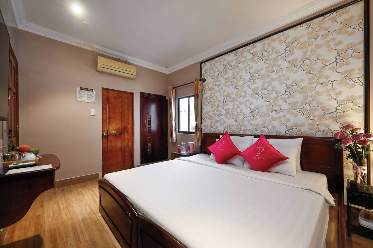 Quarto de hotel com cama, escrivaninha, guarda-roupa e ar condicionado fixado na parede.