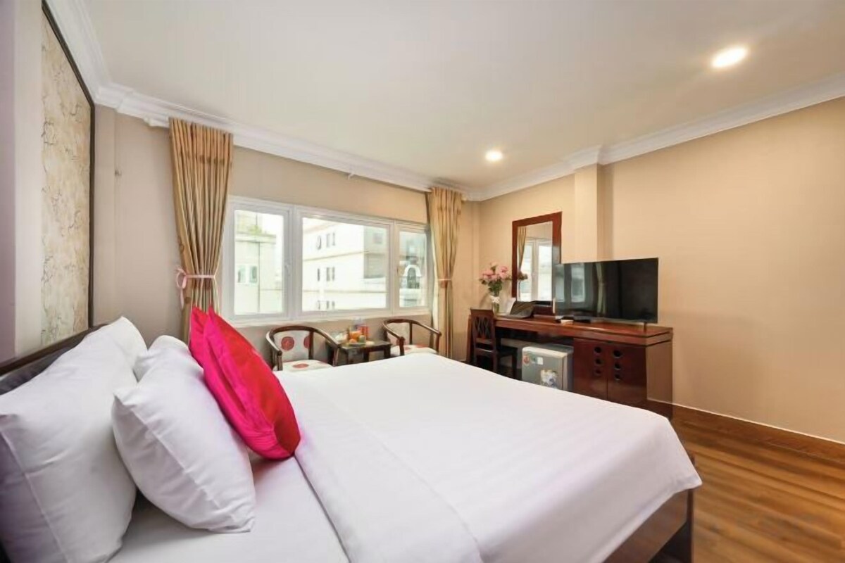 A hotel room with a bed, a television, a desk with a chair, and a window.