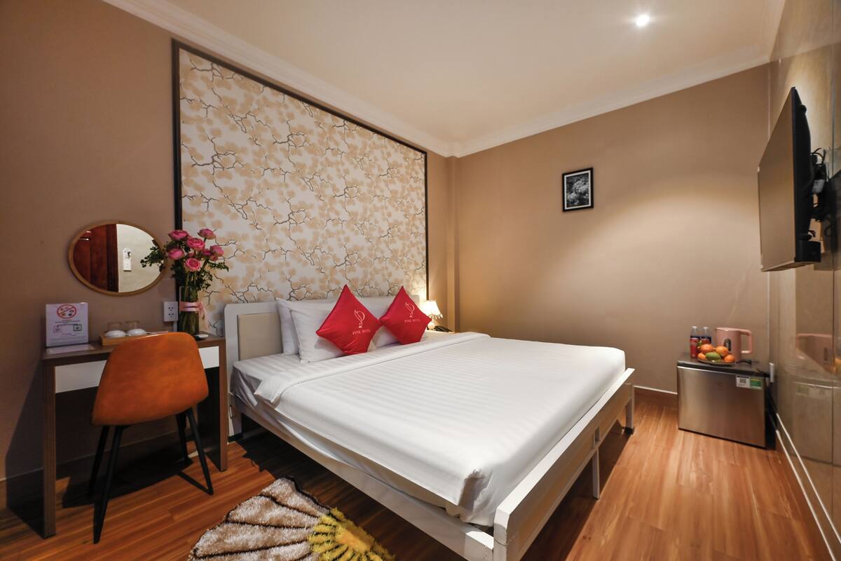 Quarto com cama, escrivaninha, cadeira, espelho, televisão fixada na parede e um pequeno frigorífico.
