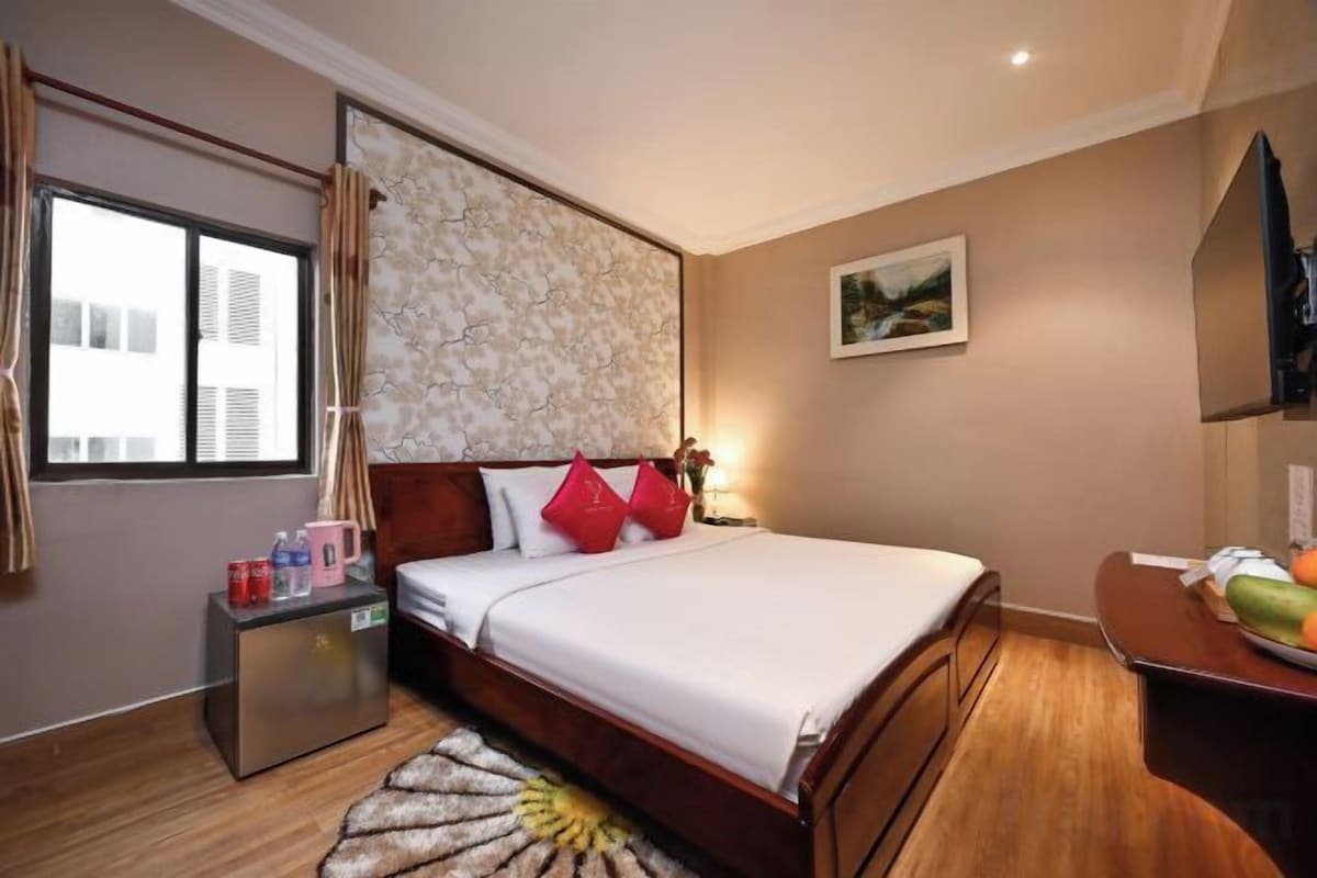 A hotel room with a bed, bedside table, lamp, and a window with curtains.