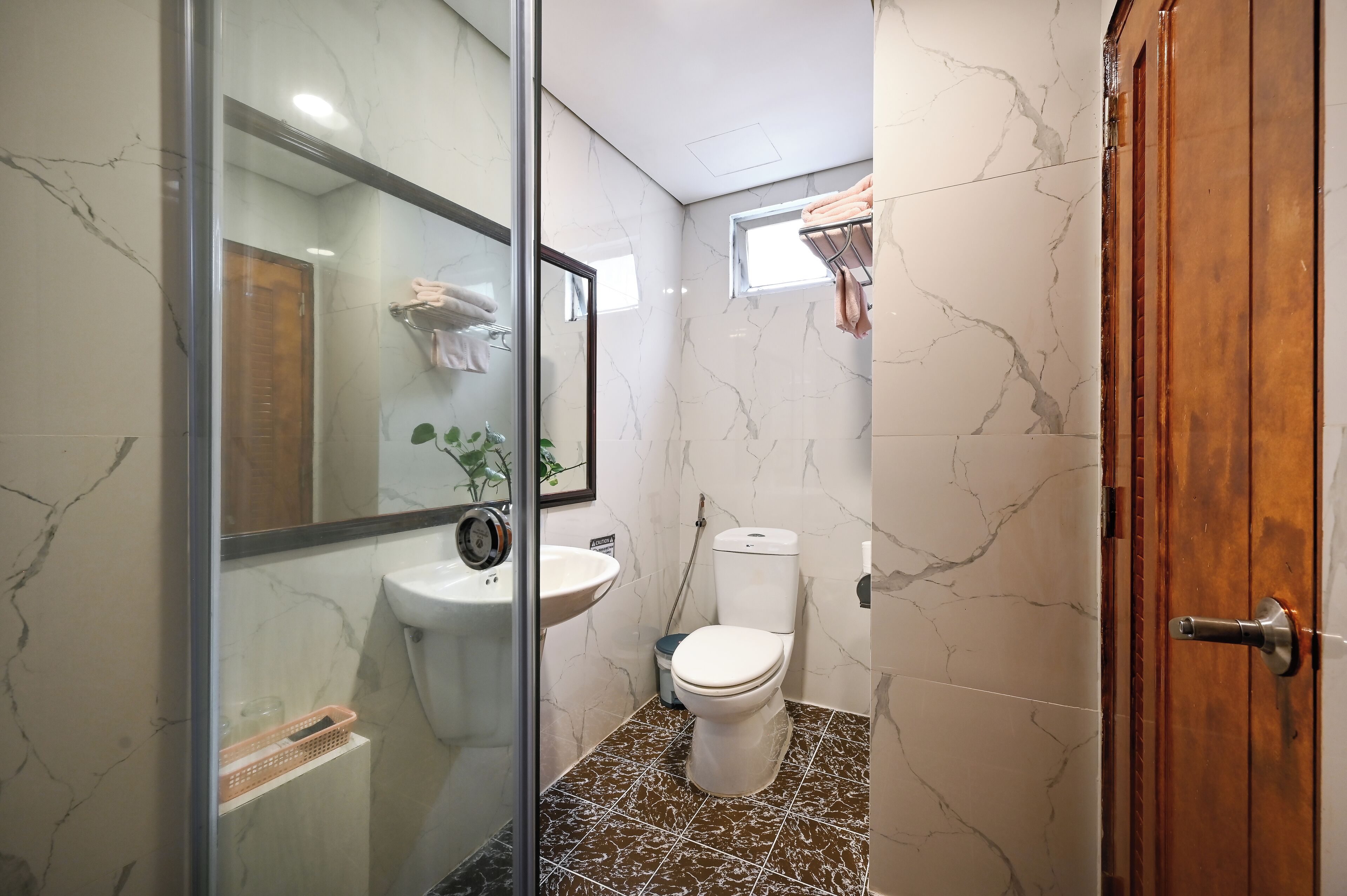 A bathroom with a glass shower enclosure, a sink, a toilet, and a small window.