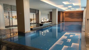 Una piscina interior moderna con una superficie de agua azul cristalina, rodeada de elementos de diseño contemporáneos y un cartel de prohibido fumar.