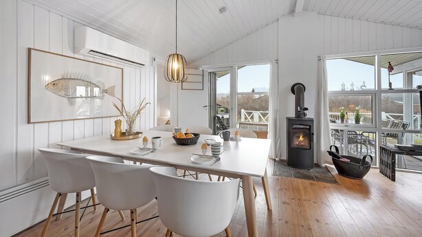 A modern kitchen with a large island, white chairs, a hanging light fixture, and a view through large windows. - Charming holiday home close to the North Sea and Søndervig center (Ringkøbing)