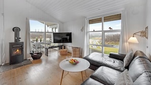 A modern living room with a fireplace, a sofa, a coffee table, and a TV. - Charming holiday home close to the North Sea and Søndervig center (Ringkøbing)