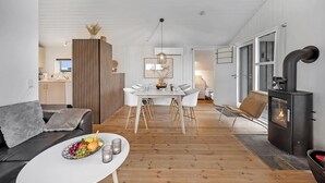A modern living room with a dining area, a black wood-burning stove, and a grey sofa. - Charming holiday home close to the North Sea and Søndervig center (Ringkøbing)