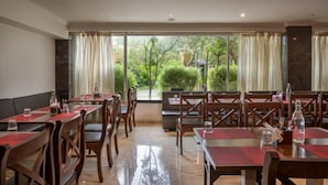 A restaurant with tables and chairs, large windows with curtains, and a view of greenery outside. - Aveda Diwatel (Mawal)