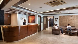 A reception area with a wooden reception desk, a wall with artwork, and a seating area with sofas and a coffee table. - Aveda Diwatel (Mawal)