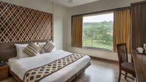 A hotel room with a bed, a desk, a chair, a ceiling fan, and a window with curtains. - Aveda Diwatel (Mawal)