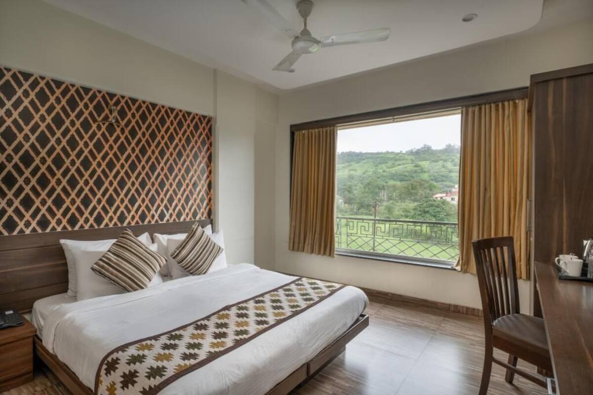 A hotel room with a bed, a desk, a chair, a ceiling fan, and a window with curtains.