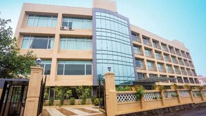 A multi-story hotel with a curved glass facade, a gated entrance, and a landscaped courtyard. - Aveda Diwatel (Mawal)