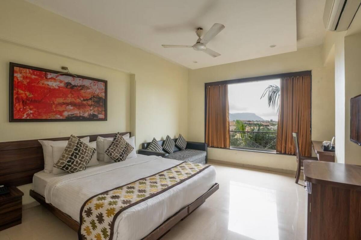 A hotel room with a bed, a sofa, a TV, and a balcony with a view.