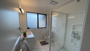 Een moderne badkamer met een douchecabine van glas, een toilet en een wastafel met een klein plantje op het aanrecht.