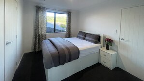 Een slaapkamer met een bed, een nachtkastje, een raam met gordijnen en een deur.