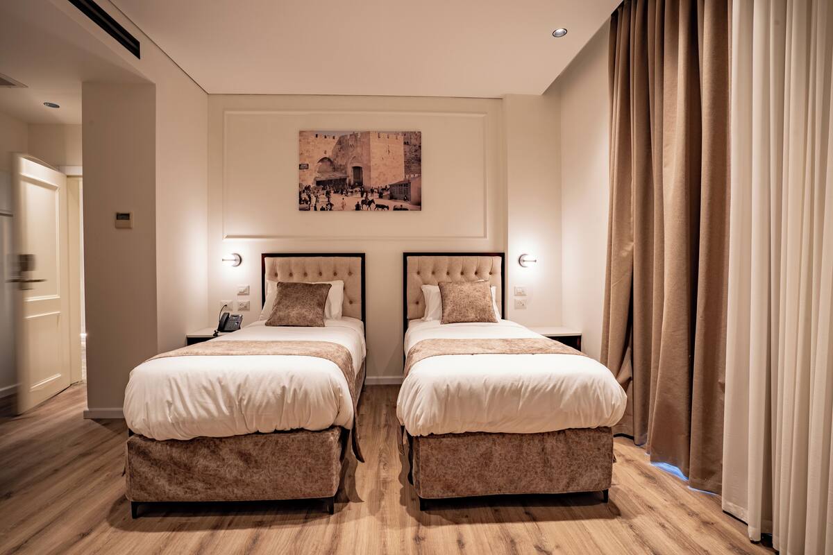 A hotel room with two beds, a large painting above the beds, and a view of the city through the window.