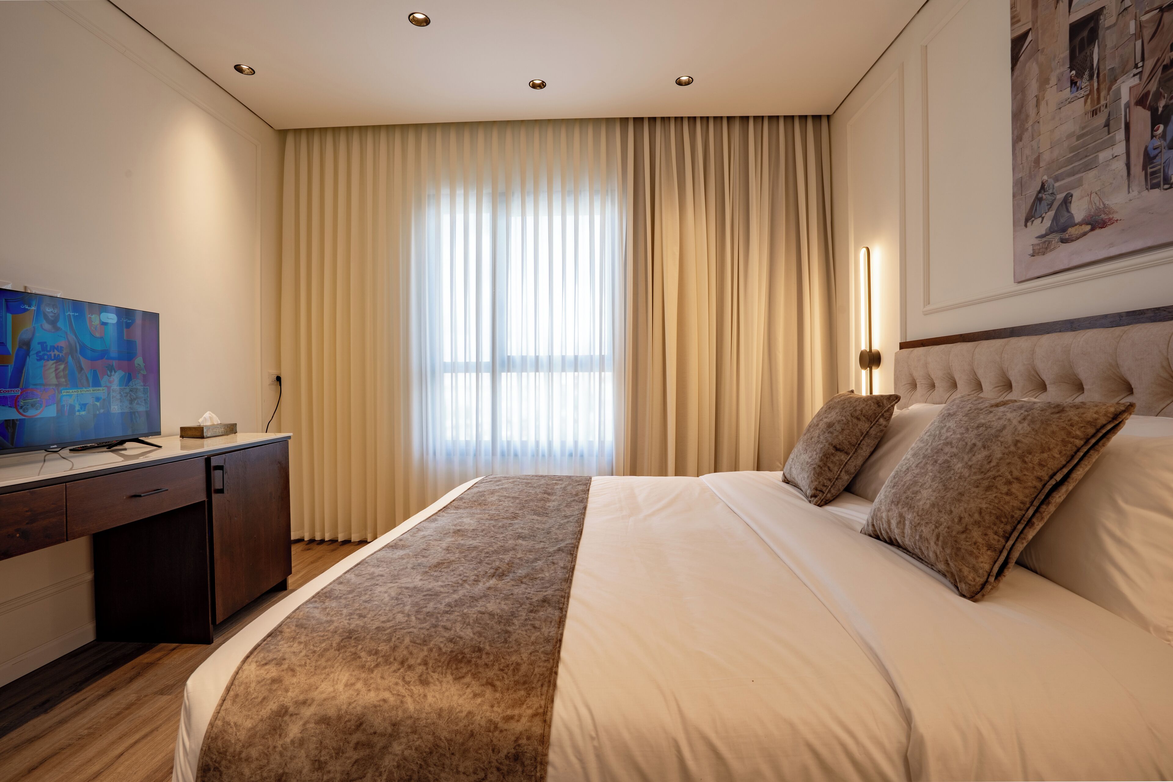 Una habitación de hotel con una cama grande, un escritorio con televisor y un cuadro en la pared.