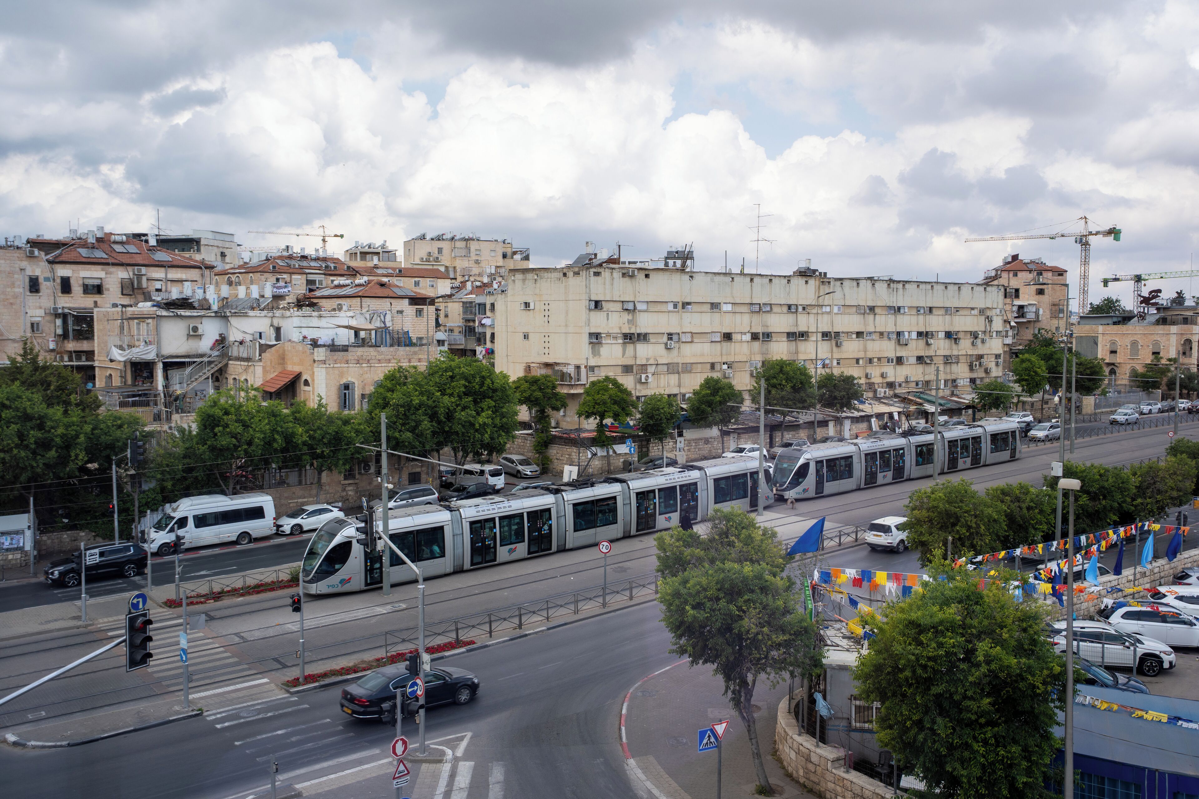 A tram line with a modern train, a road with cars, and buildings in the background.