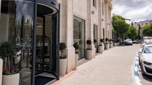 A hotel entrance with a revolving door, potted plants, and a clear sky.