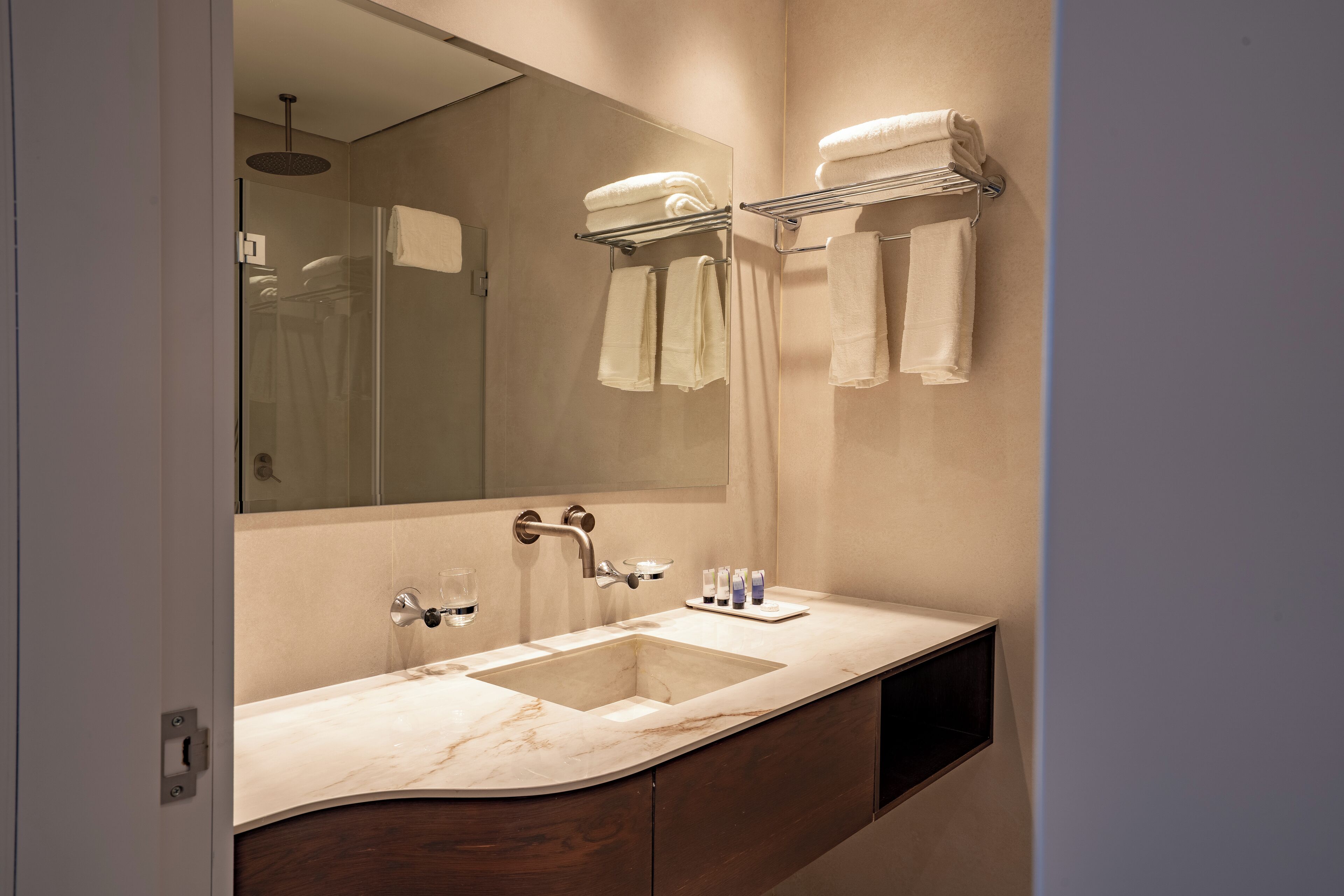 Un baño moderno con un lavabo de mármol, un espejo grande y un perchero para toallas.
