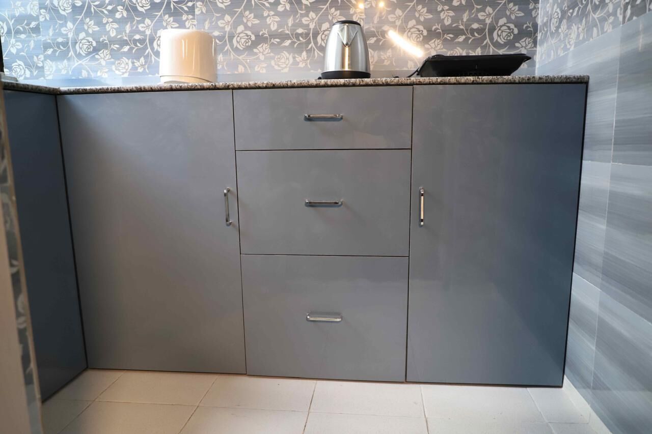 A kitchen with grey cabinets, a countertop, and a kettle.