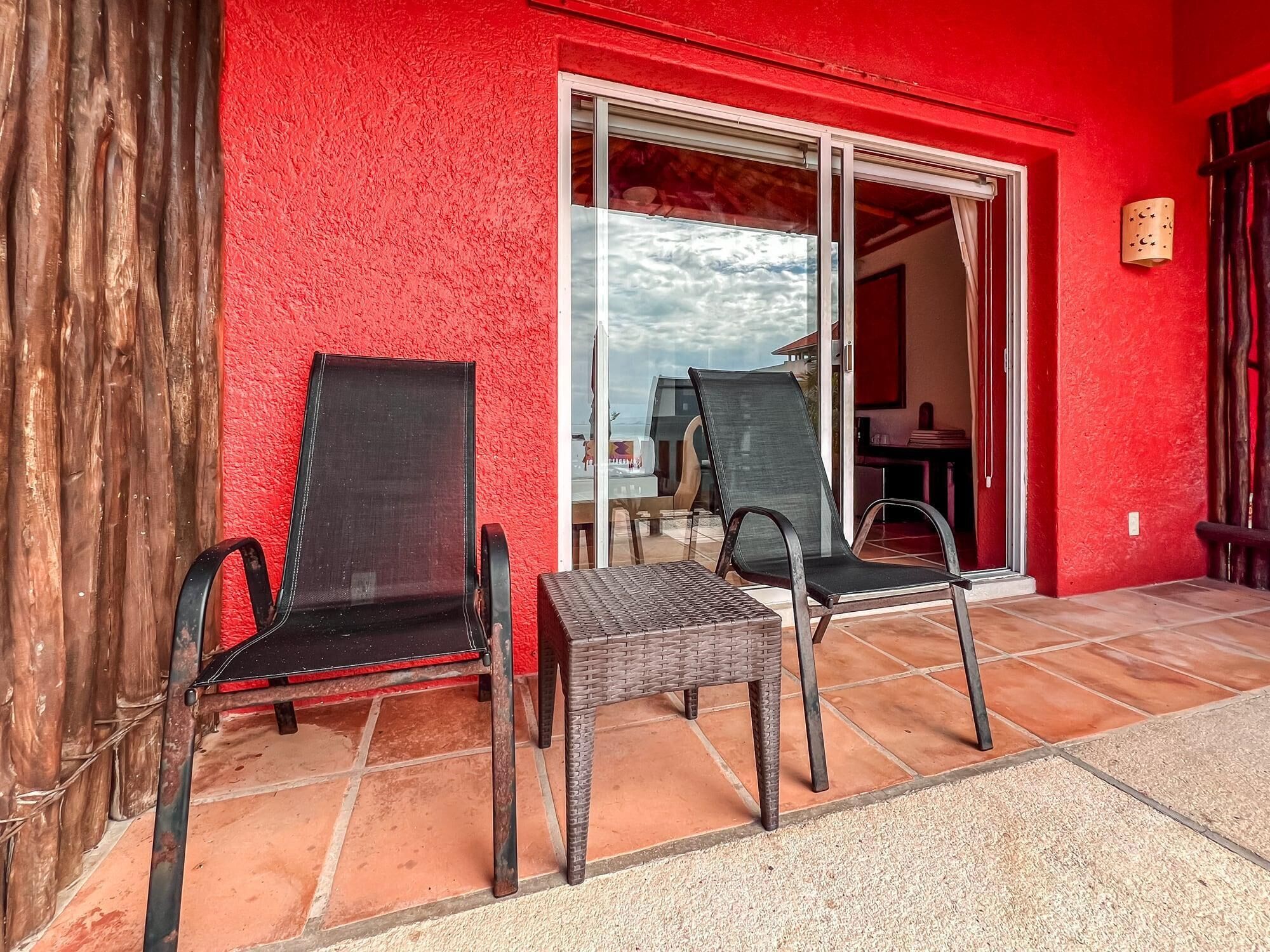 A red building with a patio area featuring two black chairs and a small table.