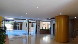A hotel lobby with a glass entrance, a central yellow pillar, and a staircase.