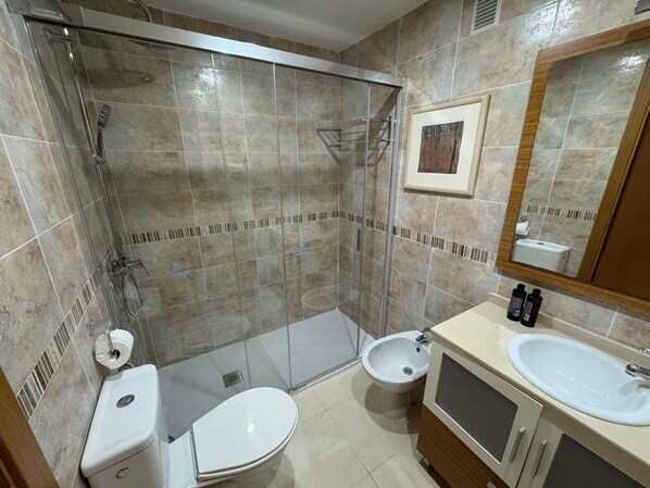 A modern bathroom with a glass-enclosed shower, a toilet, a bidet, and a sink with a mirror.