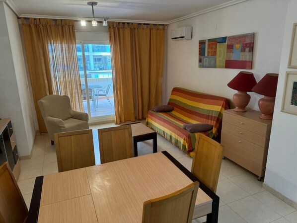 Una sala de estar con sofá, sillón, mesa de madera y un balcón con cortinas.