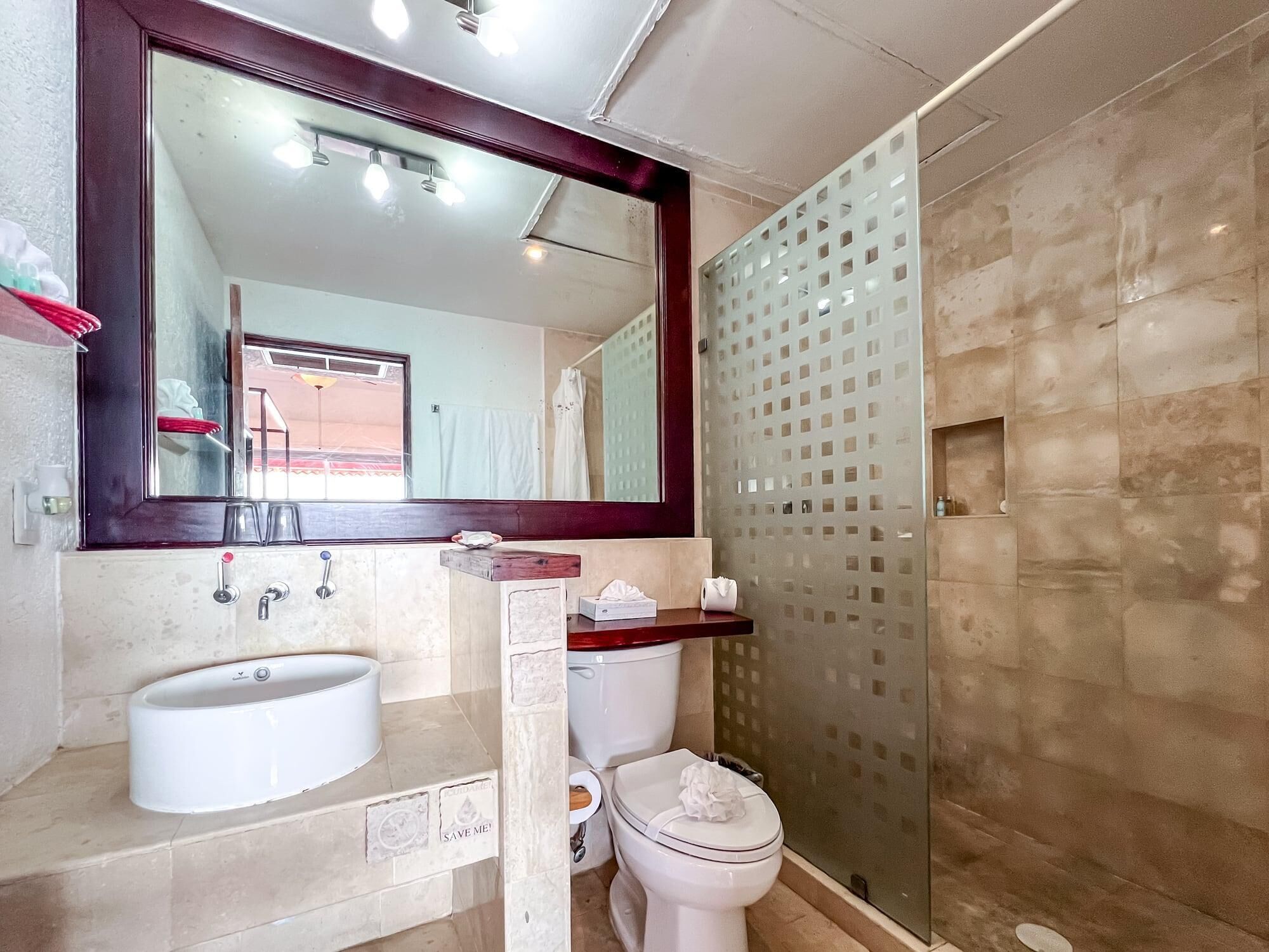 A bathroom with a large mirror, a sink, a toilet, and a shower area.