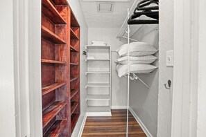 A narrow walk-in closet with wooden shelves on the left and white shelves on the right, a white door, and a white wall.