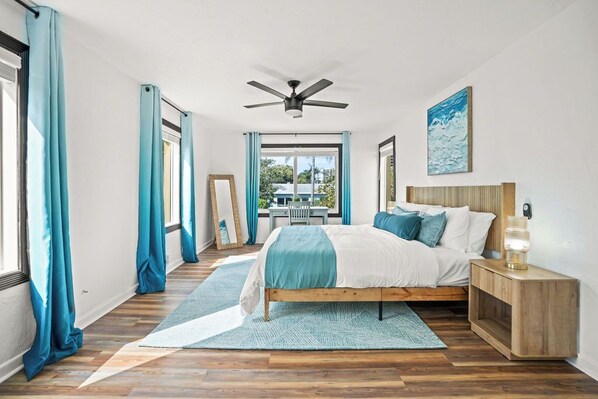 A bedroom with a bed, a nightstand, a ceiling fan, and a view of the outdoors.
