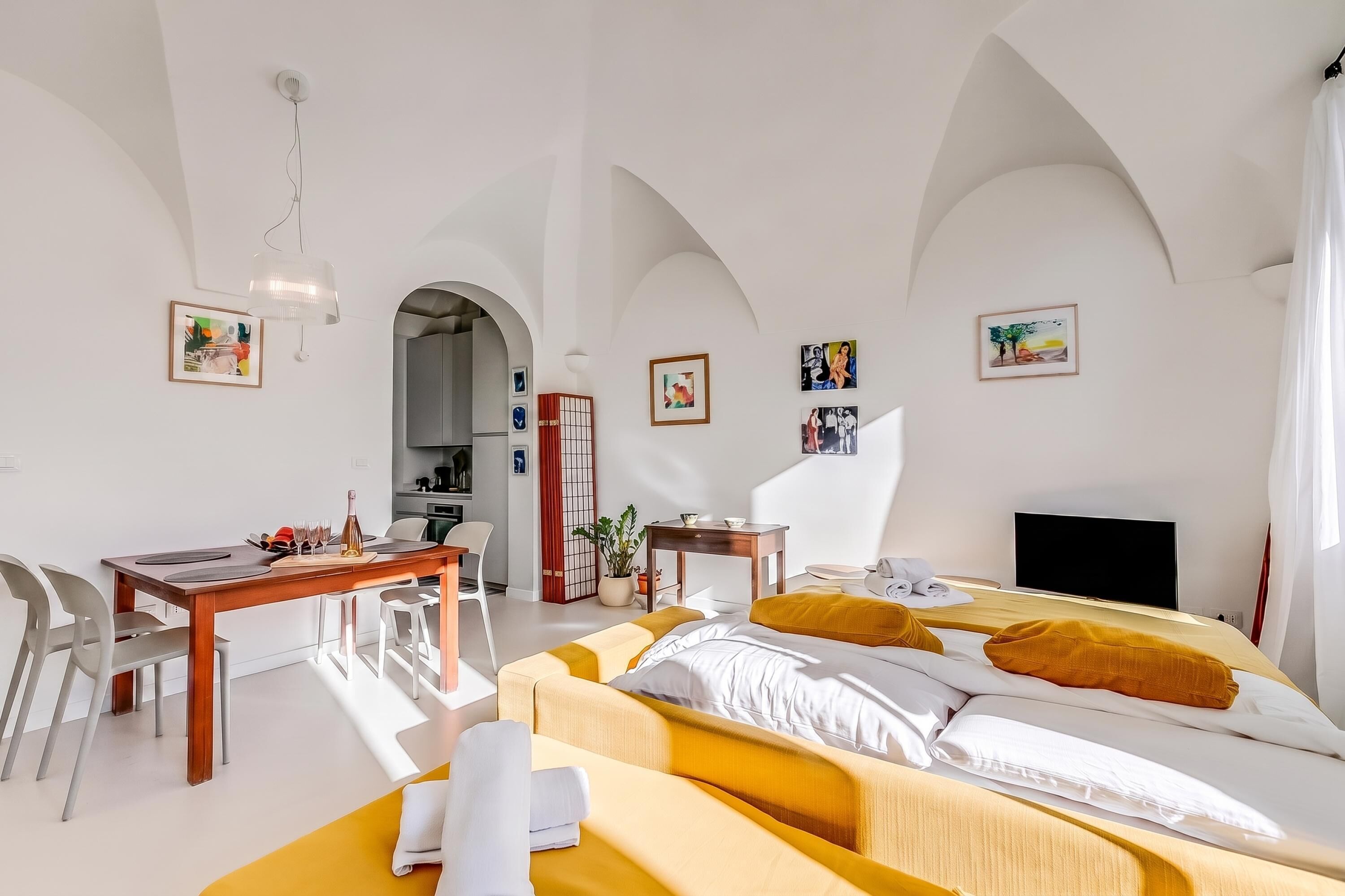A modern hotel room with a bed, a desk, a chair, a TV, and artwork on the walls.