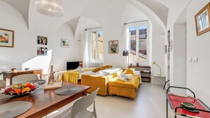 A spacious room with a dining area, a sofa set, and a bed with yellow bedding.