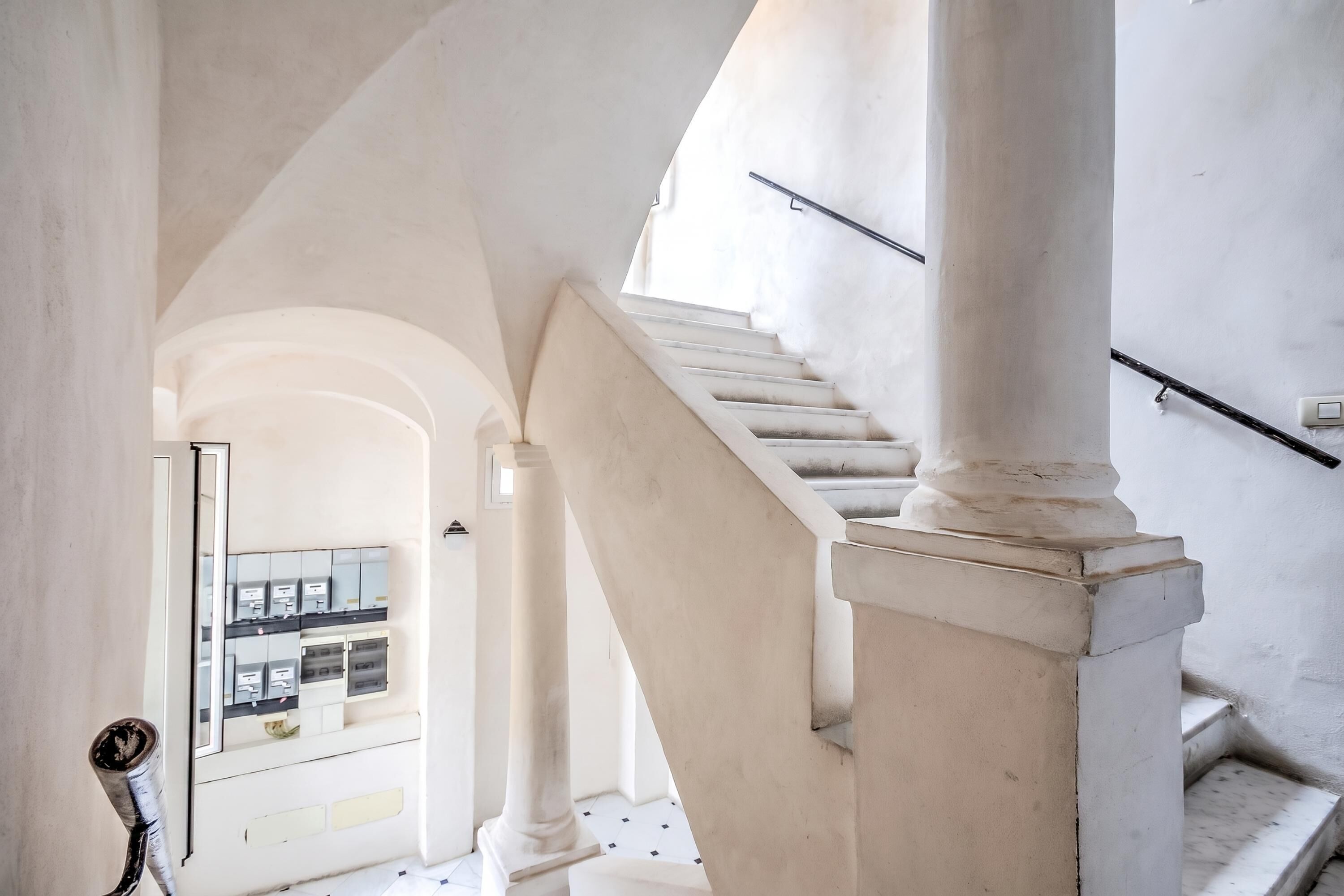 Un escalier orné de colonnes blanches et doté d’une rampe, menant à un niveau supérieur avec un balcon.