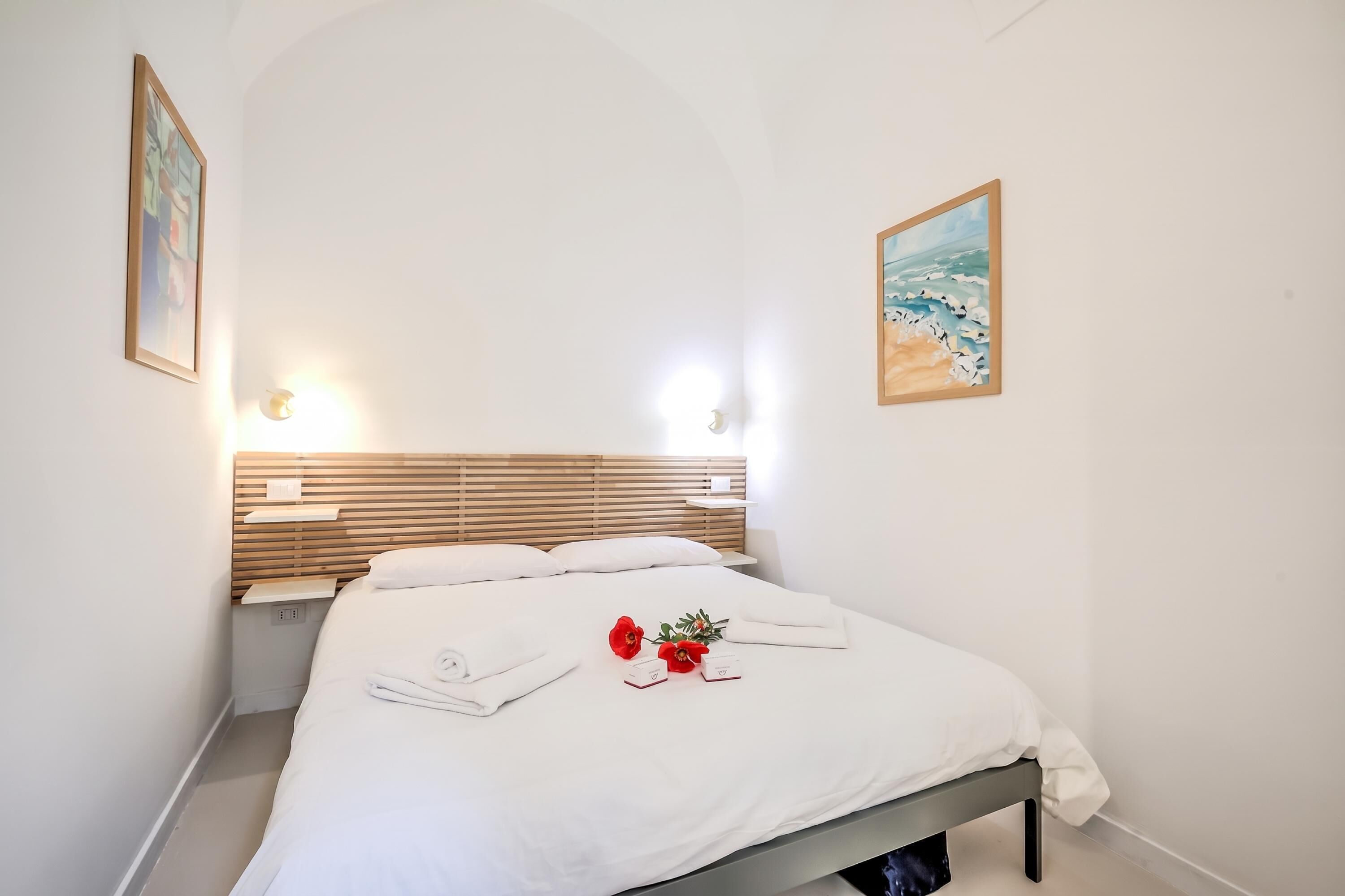 A hotel room with a bed, a wooden headboard, two wall-mounted lights, and two framed pictures.