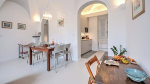 Zona pranzo con tavolo e sedie in legno, cucina sullo sfondo e corridoio che porta a un'altra stanza.