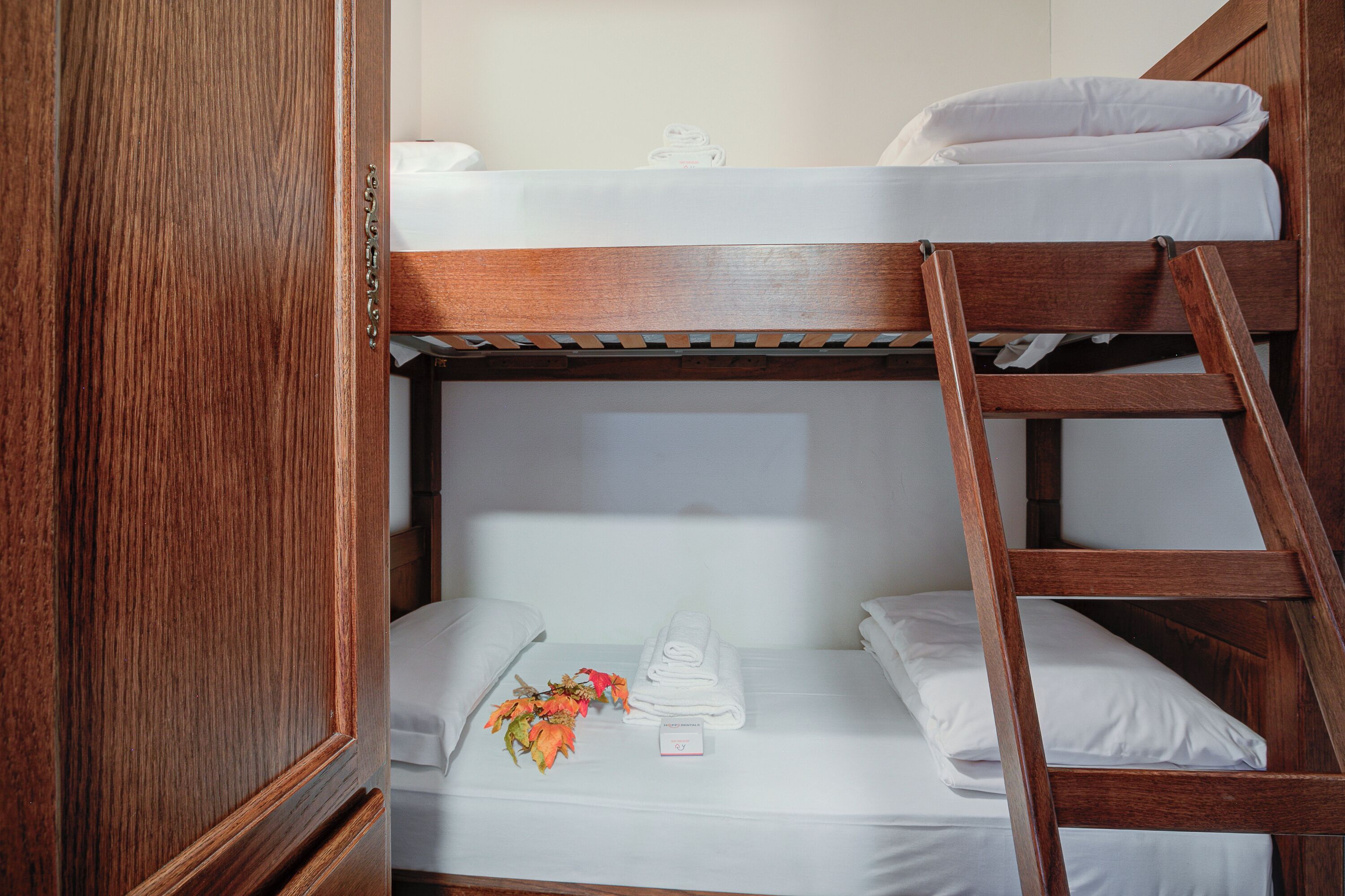 Un lit superposé avec une literie blanche, une échelle en bois et un arrangement floral sur le lit du bas.