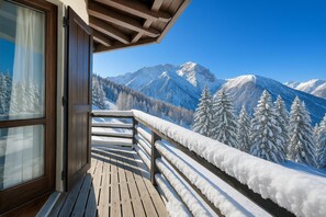 Varanda de madeira com vista para montanhas e árvores cobertas de neve.