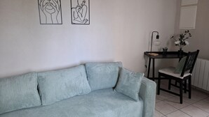 Una habitación con un sofá azul claro, una mesa de comedor de madera con una silla, y dos obras de arte enmarcadas en la pared.