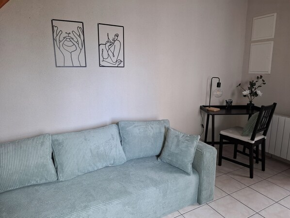 A room with a light blue sofa, a wooden dining table with a chair, and two framed artworks on the wall.