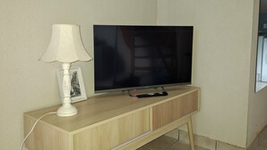 Un televisor sobre un soporte de madera, con una lámpara blanca y un marco de foto a un lado.