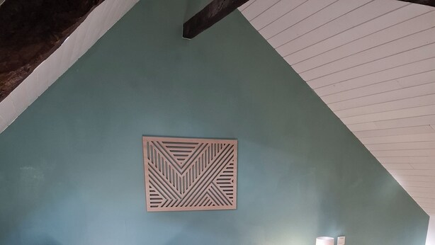 Un dormitorio con techo inclinado, una cama con ropa de cama blanca, dos mesitas de noche con lámparas y un elemento decorativo en la pared.